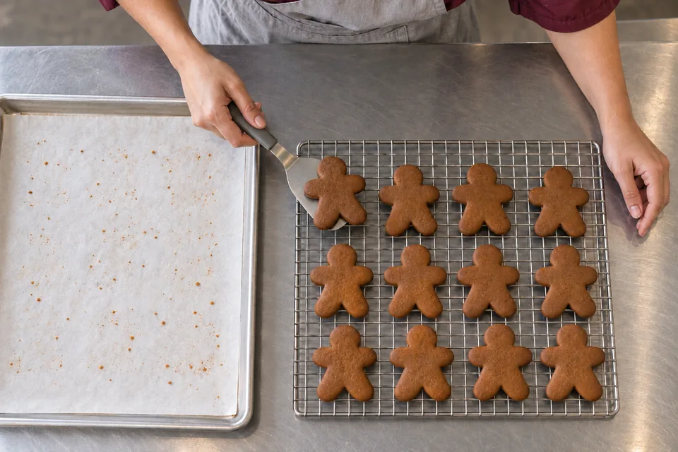 A cook transfers baked gingerbread cookies to a cooling rack.