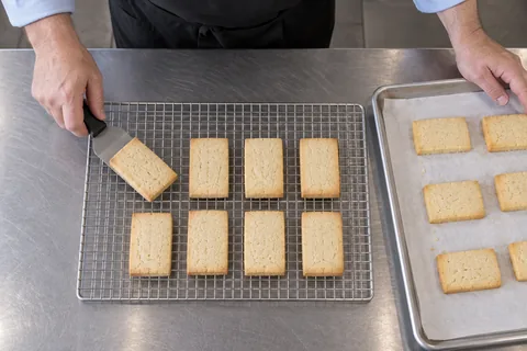 Rectangular shortbread transferring from a cooled tray to a wire rack.