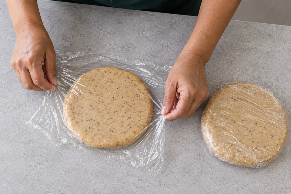 Hands wrap two flat discs of speckled cookie dough.